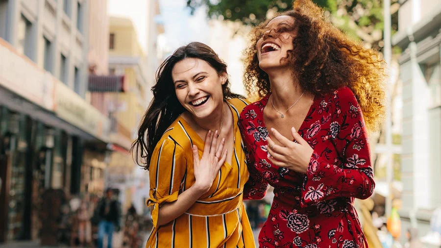 Two fashionable millennial women walking down a city street and laughing.